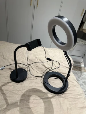 Ring light och en mobilhållare svart - Säljer en svart ring light och justerbar mobilhållare. Perfekt för att skapa content, streama eller ta selfies. Lampan har rund form och drivs via USB. Båda stativen är flexibla och kan vinklas efter behov. Stilren design i plast och metall.