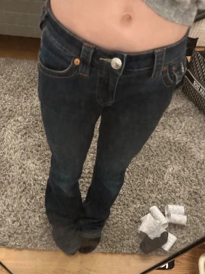 Mörkblå True Religion jeans bootcut - Säljer ett par mörkblå jeans från True Religion med klassiska kontrastsömmar och ikonisk bakficka med lock och knapp. Modellen är Becca. De är bootcut. STORLEK W24 jätte bra skick endast lite upptrampat på ena byxlängden (se bild) 