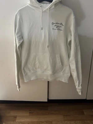 Vit från zara - Snygg vit hoodie från zara Atelier med broderad text på bröstet och ryggen. Klassisk känguruficka framtill, justerbar huva med dragsko och ribbade muddar. Perfekt för dig som vill ha en clean och exklusiv look.