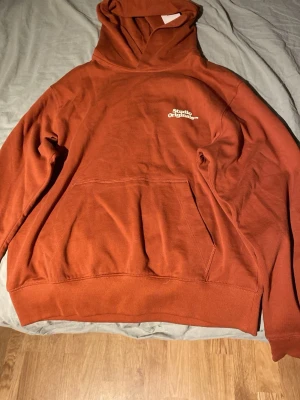 Rostbrun hoodie från Jack & Jones - Snygg rostbrun hoodie från Jack & Jones med trycket 'Studio Originals' på bröstet. Klassisk känguruficka framtill och ribbade muddar. Perfekt för dig som gillar en avslappnad och trendig stil. Tillverkad i mjuk bomull för extra komfort. Ny pris 600kr aldrig använd lappen sitter kvar.