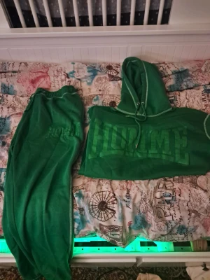 Grönt loungewear-set med hoodie - Mysigt grönt loungewear-set med matchande hoodie och byxor. Hoodien har dragsko och trycket 'HOMME' framtill. Byxorna har resår i midjan och samma tryck på benet. Perfekt för chill dagar hemma eller när du vill vara extra bekväm.