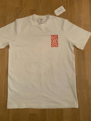 Vit t-shirt från Casablanca - Snygg vit t-shirt från Casablanca med rött tryck på bröstet. Klassisk rund hals och korta ärmar. Tillverkad i mjuk bomull för skön känsla och stilren look. Perfekt till jeans eller shorts för en clean outfit.