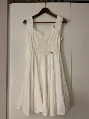 Vit kort spetsklänning - Söt vit klänning med spetsdetaljer upptill och v-ringad hals. Kjolen är lätt utsvängd och klänningen har en dekorativ dragkedja i ryggen. Perfekt för sommarens alla tillfällen. Materialet känns som bomull och spets. Klänningen är från Bubbelrooms studentklännings kollektion från några år tillbaka och är i storlek Xs. Enbart använd en gång 