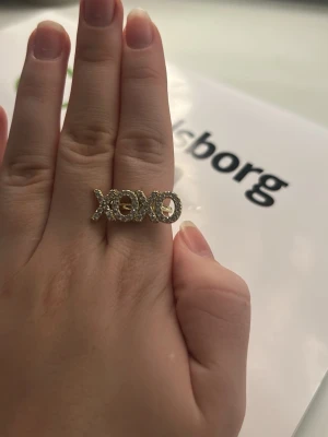 Guldig XOXO-ring med stenar - Unik ring i guldton med texten 'XOXO' täckt av gnistrande stenar. Ringen har inte kommit till användning där ja säljer kostar 500 ny 😛❤️