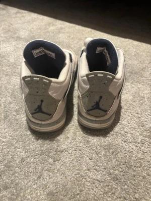 Nike Air Jordan 4 Retro vit/blå - Säljer ett par Nike Air Jordan 4 Retro sneakers i vitt med marinblå detaljer och specklad häl. Klassisk siluett med snörning, rund tå och meshpaneler. Sköna och ikoniska sneakers som passar perfekt till streetwear-stilen.  Har låda till skorna!