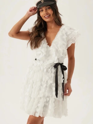 Vit volangklänning med svart knytband - Superfin vit kortklänning med volanger och v-ringning. Klänningen har ett svart knytband i midjan som går att ta bort och är ärmlös med lager på lager-effekt. Perfekt för student eller sommarens alla tillfällen. Aldrig används, köptes förra månaden inför studenten men passar inte längre. Orginal pris 1199, köpt från bubbelroom.
