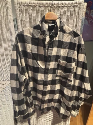 Svartvit rutig skjorta från ASOS - Klassisk svartvit rutig skjorta med bröstficka och knappar framtill. Skjortan har lång ärm och avslappnad passform, perfekt för en chill och stilren look. Tillverkad i mjuk bomull som känns skön mot huden.