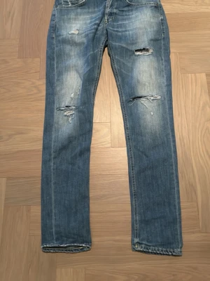 Blå slitna straight jeans - Säljer ett par blå jeans med slitningar och hål på framsidan. Jeansen har en rak passform och klassisk femficksdesign. Perfekta för en avslappnad och trendig look. Materialet är klassisk denim i bomull. Använd 2 ggr kom med ett pris 