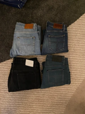 Fyra par jeans i olika färger från tiger of sweden  - Säljer fyra par jeans i olika tvättar: ett par ljusblå, ett par mörkblå, ett par svart och ett par mellanblå. Klassisk femficksmodell med raka ben och skinnpatch bak i midjan. Perfekta basjeans för alla tillfällen och enkla att matcha med olika stilar. 4st bulk tiger of sweden jeans 