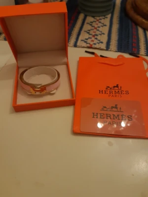 Rosa armband från Hermès - Säljer ett exklusivt rosa armband från Hermès med guldfärgat spänne. Armbandet har en elegant och stilren design och kommer i originalförpackning med tillhörande Hermès-påse. Perfekt accessoar för dig som gillar lyxiga detaljer.