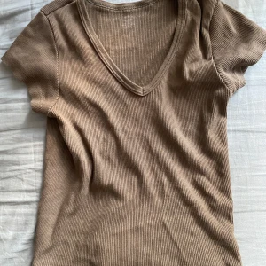 Brun topp Brandy Melville - Ribbad Brun topp från Brandy Melville med v-ringning och korta ärmar. Skön och stretchig i bomullsmix, perfekt till jeans eller kjol. Väldigt söt nu till hösten! Säljer då den är för liten för mig och inte används 🩷