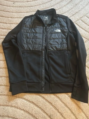 Svart cardigan från The North Face - Snygg svart cardigan från The North Face med hög krage och dragkedja framtill. Tröjan har logga på bröstet och är tillverkad i ett mjukt, sportigt material som passar perfekt till både chill och aktivitet. Köpte på XXl ca 1400kr på rea så detta är nyaste modellen. I nyskick haft på mig endast 3 ggr. Passar även S. Använd gärna köp nu❤️