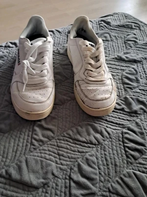 Vita sneakers från Fila med svart detalj - Jag säljer ett par Fila-skor som är i acceptabelt skick, trots att de är lite slitna på vissa ställen. De kan fortfarande användas och är perfekta för dig som vill ha ett par bekväma skor till ett lågt pris.  Jag säljer dem för 90 kr. Jag är öppen för snabba affärer!  Tveka inte att höra av dig om du är intresserad eller har några frågor. Först till kvarn gäller!