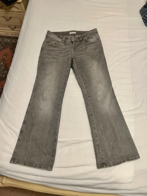 Grå bootcut jeans från gina Tricot - Säljer ett par grå low waist bootcut jeans från Gina Tricot i storlek 40. Jeansen har klassisk femficksdesign, dubbla knappar i midjan och bakfickor med lock och knapp. Materialet är slitstarkt denim i bomull och passformen är relaxed med utsvängda ben.