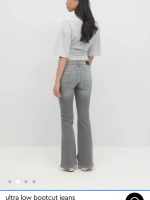 Grå bootcut jeans med låg midja Gina Tricot - Säljer dessa snygga grå bootcut jeans med låg midja och klassiska fickor både fram och bak. Jeansen har en lätt utsvängd passform nertill och är perfekta för dig som gillar en retro vibe. Tillverkade i mjukt denimtyg för en bekväm känsla. Endast använt de en gång, de är så gott som nya.