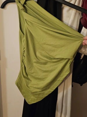 Grön oneshoulder topp - Snygg grön oneshoulder topp med draperad passform och lätt rynkade detaljer på sidan. Perfekt för dig som vill sticka ut med en cool och trendig look. Asymetrisk längst mer. 