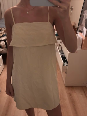 Sommarklänning - Söt ljusrosa klänning med tunna axelband och volangdetalj upptill. Klänningen är kort och har en rak passform, perfekt för varma dagar. Tillverkad i ett lätt tyg som känns luftigt och bekvämt.