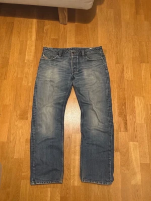 Vintage Diesel Jeans - Säljer ett par klassiska blå Diesel Larkee jeans med raka ben och snygg slitning. Jeansen har fem fickor, tydliga sömmar och patch bak i midjan. Tillverkade i tåligt denim med en relaxed fit som ger skön känsla hela dagen. Storleken passar cirka 34/32