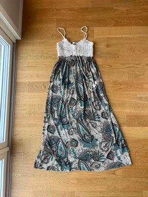 Maxiklänning i bohemisk stil från Cecilia H - Maxiklänning från Cecilia H, fungerar även som strandklänning. Superfin virkad överdel med ”hängen”, kjolen har en skönt glansigt material. Är i fint skick och har inte hittat några skavanker. Hittar inte storlekslapp men skulle uppskatta att den är en XS/S.
