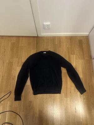 Svart stickad tröja  - En enkel svart stickad tröja med rund hals och långa ärmar. Tröjan har ribbstickade muddar vid ärmslut och nederkant. Passar perfekt till lager-på-lager och funkar året runt. Materialet ser ut att vara mjukt och bekvämt.