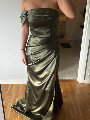 Olivgrön balklänning med slits - Säljer min balklänning som aldrig kom till användning då den va en storlek förstor. Köpt från en hemsida i Albanien