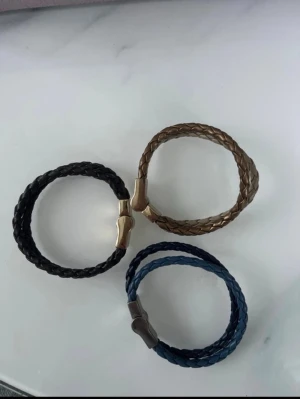 Flätade armband 3 stycken  - Stilrent svart armband i flätat läder med ett magnetiskt spänne i metall. Perfekt accessoar för en cool och avslappnad look. Passar både till jeans och skjorta. Färgen guld, svart och mörk blå alla tre ingår för 35 kr 