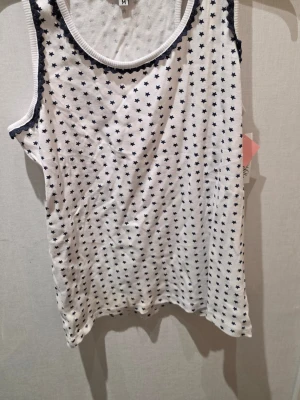 Vit linnetopp med stjärnmönster Miss Milla - Snygg vit linnetopp från Miss Milla med små marinblåa stjärnor över hela tyget. Toppen har ribbad struktur och marinblåa dekorativa kanter vid halsringning och ärmhål. Perfekt för en avslappnad och trendig look.