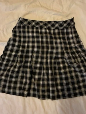 Svartvit rutig kortkjol - En svartvit rutig kortkjol med klassiskt rutmönster och lätt utställd passform. Kjolen har en markerad midja och är perfekt för en trendig och ungdomlig stil. Passar till många olika outfits och är enkel att matcha.