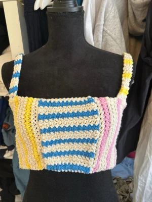 Randig virkad linnetopp i pastell - Superfin virkad linnetopp med breda axelband och färgglada ränder i blått, gult, rosa och vitt. Perfekt för sommaren och ger en riktigt söt och lekfull vibe. Toppen är croppad och har en mjuk, stickad känsla.