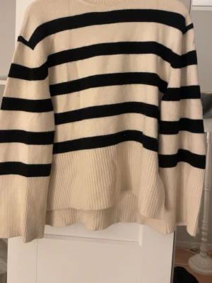 Randig stickad tröja från BikBok - Snygg stickad tröja från BikBok i beige med breda svarta ränder. Tröjan har en avslappnad passform, rund halsringning och ribbade muddar. Perfekt för en trendig och bekväm look.