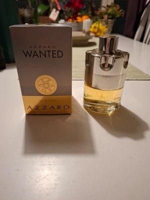 Azzaro Wanted Eau de Toilette - Azzaro Wanted Eau de Toilette med en unik, cylinderformad flaska i silverfärgad metall och glas. Doften kommer i en elegant förpackning med guld- och silverdetaljer. Perfekt för dig som gillar exklusiva och moderna parfymer.