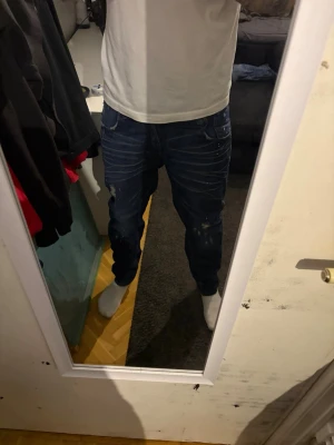 Mörkblå jeans med slitningar från G-Star - Säljer ett par gstar raw mörkblå jeans med slitna detaljer och vita färgstänk. Jeansen har normal passform och klassisk femficksdesign. Snygga kontrastsömmar och låg midja ger en avslappnad look. Perfekta till en streetwear-outfit. w31 l32
