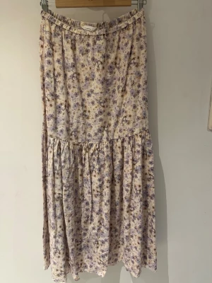 Blommig långkjol i linneblandning H&M storlek S-Ny! - Långkjol från H&M i en ljus linneblandning med blommigt mönster i lila och beige toner. Kjolen har en avslappnad passform med resår i midjan och volangdetalj nedtill. Perfekt för en somrig och chill look.