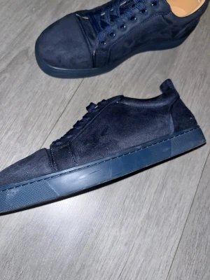 ”Utan låda” Mörkblå  Louboutins - Lådan är inte tillgänglig säljer bara skorna.                                                 Snygga mörkblå sneakers från Louboutin i mjuk mocka med matchande snörning och klassisk röd sula med logotyp. Skorna har en låg profil och rund tå, perfekt för dig som gillar stilrena och exklusiva sneakers.
