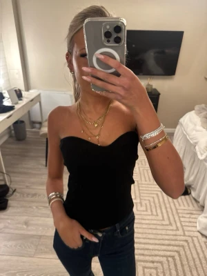 Svart bandeau tubtopp - Snygg svart bandeau tubtopp med hjärtformad urringning. Toppen är tight och sitter på plats utan axelband, perfekt att styla med jeans eller kjol. Enkel och stilren design som passar till många olika looks.