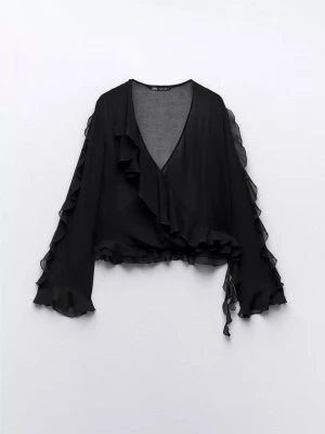 Svart omlottblus med volanger Zara - Snygg svart omlottblus från Zara oanvänd med långa ärmar och volangdetaljer längs kanterna. Blusen har knytband åt sidorna.