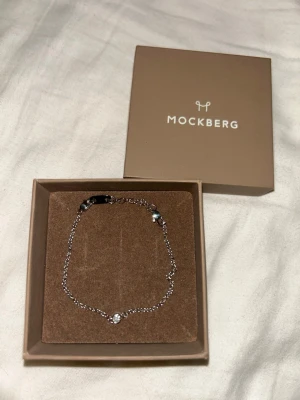 Silverfärgat armband från Mockberg - Snyggt och stilrent armband från Mockberg i silver med tunn kedja och en liten gnistrande sten i mitten. Perfekt accessoar för dig som gillar minimalistisk och elegant design. Levereras i originalask. Aldrig använt.