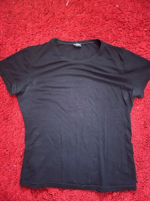 Svart t-shirt från Chanel (äkta) - En klassisk svart t-shirt från Chanel med rund halsringning och korta ärmar. Enkel och stilren design som passar till det mesta. Tillverkad i mjuk bomull för en bekväm känsla hela dagen.