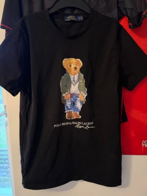 Svart Polo Bear t-shirt från Ralph Lauren - Svart t-shirt från Polo Ralph Lauren med ikoniskt Polo Bear-tryck på bröstet. Klassisk rund hals och korta ärmar. Tillverkad i mjuk bomull som känns skön mot huden. Perfekt för dig som gillar streetstyle och vill sticka ut med en cool print.