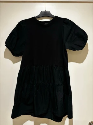 Svart kort klänning från Zara - Svart kort klänning från Zara med puffiga korta ärmar och rund halsringning. Klänningen har en volangig kjoldel och är tillverkad i ett mjukt bomullstyg. .