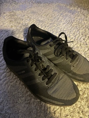 Svarta Adidas LA Trainer sneakers - Säljer ett par svarta Adidas LA Trainer sneakers med klassiska tre ränder på sidan och diskret logga på hälen. Skorna har snörning och är tillverkade i ett ventilerande syntetmaterial med meshstruktur. Perfekta för en sportig och stilren look.