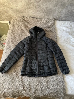 Svart dunjacka med huva från Peak Performance - Snygg svart dunjacka från Peak Performance i designen Argon Light Hood Jacket med quiltad design och huva. Jackan har dragkedja framtill och två sidofickor med dragkedja. Perfekt för kalla dagar och enkel att matcha med allt. Klassisk pufferstil som alltid är rätt. Har ett litet hål upptill kragen men är inte så synligt vid användning ☑️ 