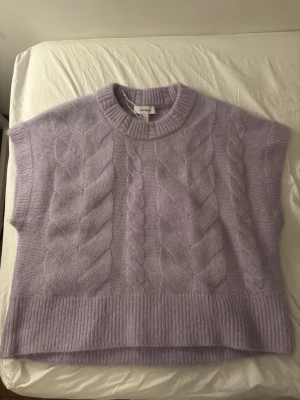 Ljuslila kabelstickad väst från other stories - Supersnygg ljuslila kabelstickad väst från other & stories. Modellen är boxy med breda axlar, ribbad kant nedtill och vid halsen. Materialet är mjukt och fluffigt, perfekt för lager på lager. Västen har ett klassiskt flätmönster framtill och baktill.