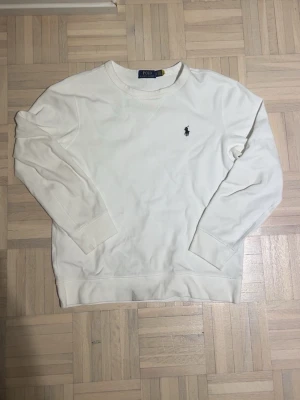 Vit stickad tröja från Polo Ralph Lauren - Klassisk vit stickad tröja från Polo Ralph Lauren med rund halsringning och den ikoniska lilla broderade loggan på bröstet. Tröjan har långa ärmar och ribbade muddar vid ärmslut och nederkant. Perfekt för en clean och stilren look. Äkta Ralph Lauren tröja, kvitton finns måste bara leta fråga om ni behöver. Har lite missfärg som kommit från tvätten nångång som syns i bilden men man märker de knappt.