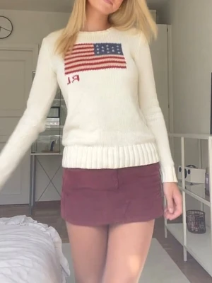 Polo Ralph Lauren- The iconic Flag Jumper - Vit stickad tröja från Polo Ralph Lauren med amerikansk flagga och RL-broderi på bröstet. Tröjan har rund halsringning, ribbade muddar och är långärmad. Perfekt för en klassisk och stilren look.