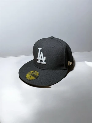 Svart LA-keps från New Era - Stilren svart keps från New Era med LA-logga broderad i vitt framtill. Klassisk 59FIFTY-modell med platt skärm och broderad New Era-logga på sidan. Kepsen är tillverkad i ett slitstarkt tyg och har MLB-logga baktill.