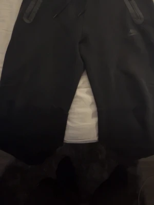 Svarta Nike tech mjukisbyxor - Säljer ett par svarta mjukisbyxor från Nike i storlek S. Byxorna har dragsko i midjan och dragkedjor på fickorna. Sköna och stilrena med en loose fit. Bra skick, pris kan diskuteras!