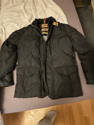 Svart dunjacka från Parajumpers - Snygg svart dunjacka från Parajumpers med klassisk krage, stora fickor och varm. Jackan har både dragkedja och knappar framtill. Inne fickor finns också. 