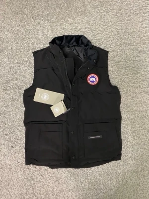 Canada gose väst M - Canada Goose väst i storlek M, sprillans ny och aldrig använd. Västen är i perfekt skick utan några defekter och kommer med tags kvar. Klassisk och stilren modell som är lätt att matcha och passar perfekt både till vardags och utomhus – håller värmen utan att kännas klumpig. Hör gärna av dig vid frågor eller om du vill ha fler bilder.
