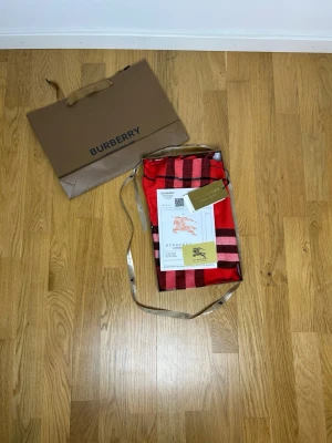 Burberry Halsduk Röd No Size 100% Kashmir - Säljer en lyxig röd halsduk från Burberry i 100% cashmere. Halsduken har klassiskt rutmönster i svart, vitt och rosa samt broderad Burberry-logga i guld. Mjuka fransar i ändarna och exklusiv känsla. Perfekt accessoar för att lyfta din outfit.
